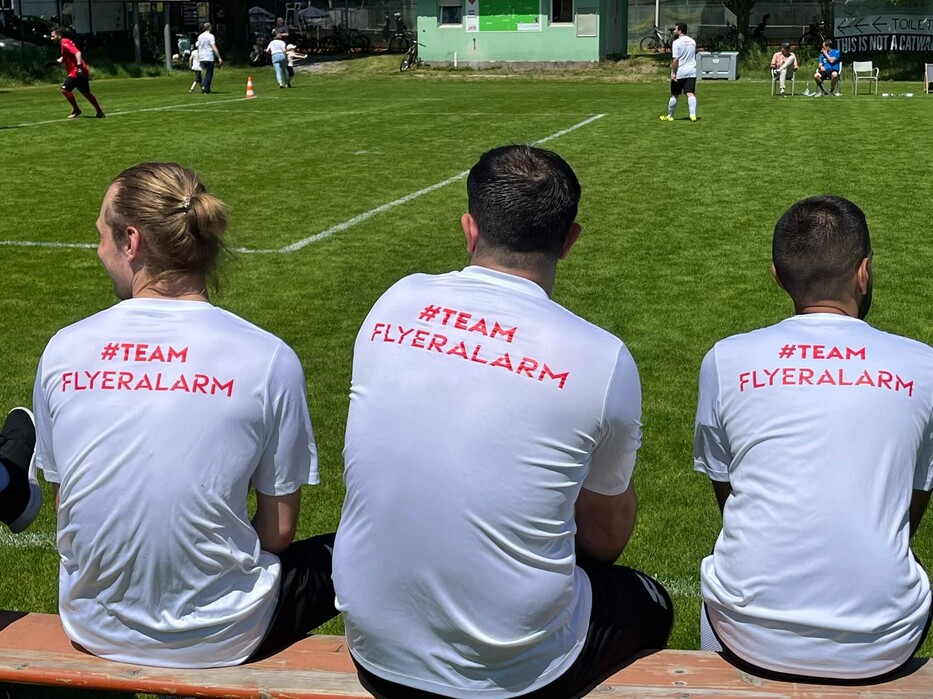 Spieler mit Team FLYERALARM-Shirts sitzen gemeinsam am Spielfeldrand.